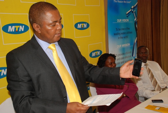 MTN CEO Themba Khumalo demonstrates how to pay water bills using MTN Mobile Money. Looking on far right is NWSC MD Dr. Richard Muhairwe
