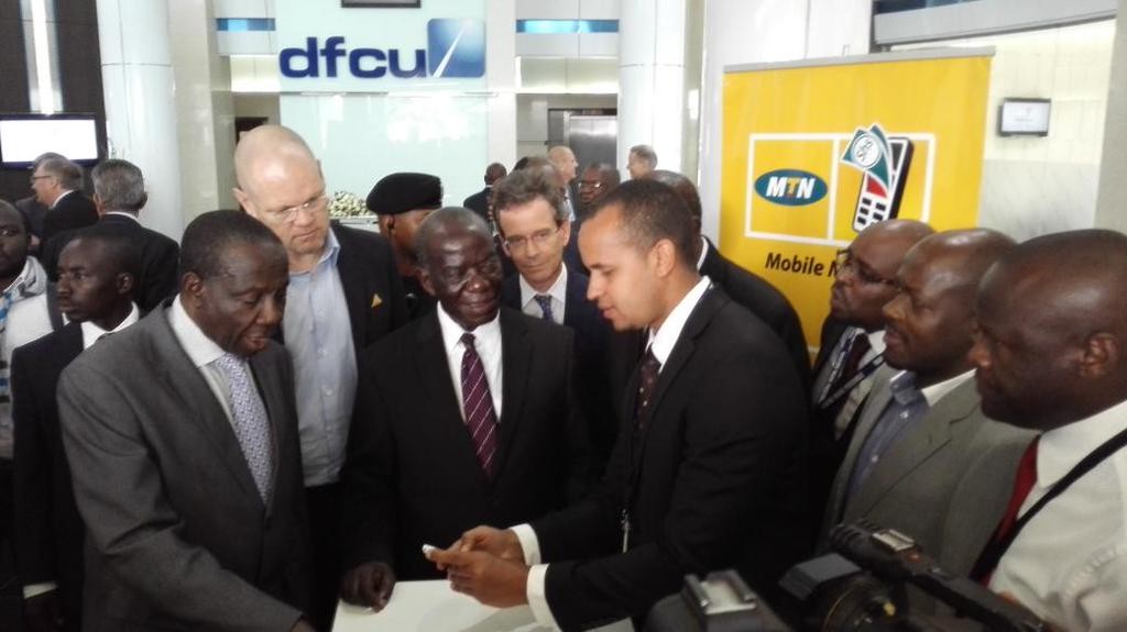 Vice President Hon. Edward Ssekandi (C), Minister of Finance Matiya Kasaijja (Extreme Left), MTN CEO Brian Gouldie (next to Kasaijja) flanked by other guests witness a demo of the service by DFCU bank official.