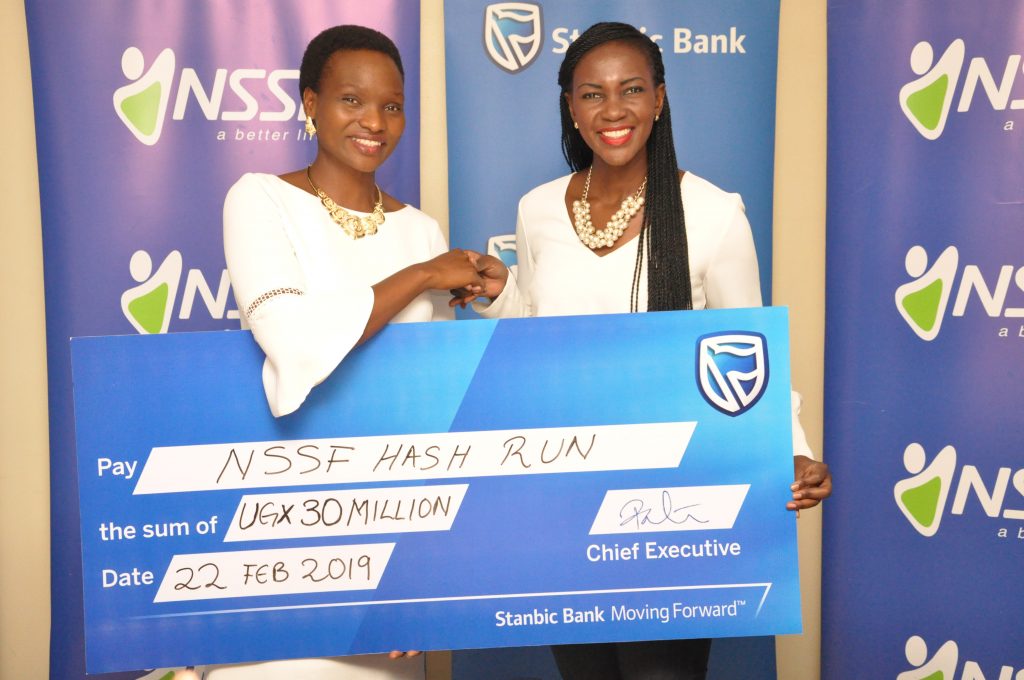 NSSF Head of Marketing and Communications, Ms Barbara Arimi (L) receiving a dummy UGX30 million cheque from Adengo Cathy, Stanbic Bank Uganda Head of Corporate Communications at a press briefing that was held at Crested Towers, Stanbic Bank Uganda Head offices on Friday 22nd, February 2019.