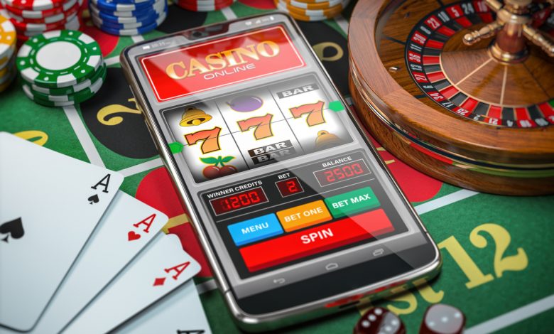 Online Casino: Smartphone or mobile phone, slot machine, dice, cards and roulette on a green table in casino. 3d illustration. (Photo by: World Financial Review)