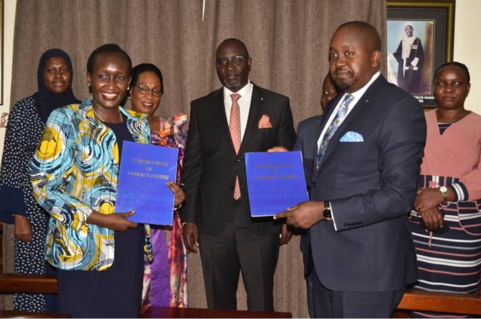UCC Ag. Executive Director, Irene Kaggwa Sewankambo (L) and the 2nd Deputy Katikkiro Owek Robert Waggwa Nsibirwa (R) display the MoUs after signing while other officials look on. (COURTESY PHOTO)