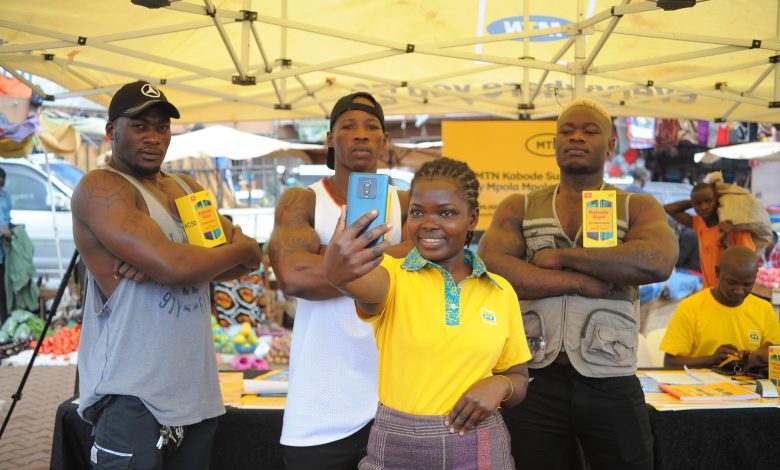 A woman poses with the newly launched the MTN Kabode Supa Smartphone, taking a selfie next to three kabode men.