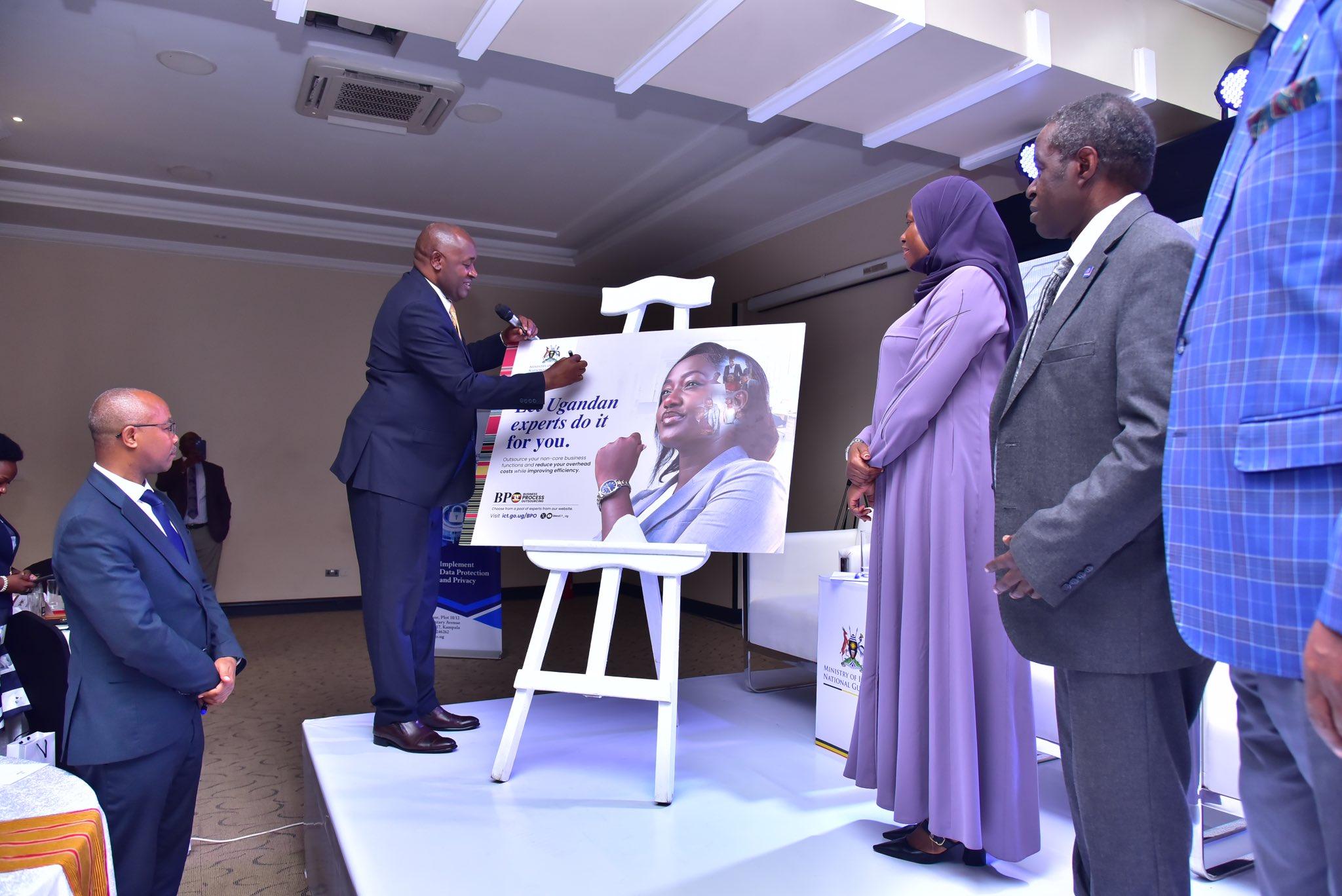 The Minister of ICT and National Guidance, Hon. Dr. Chris Baryomunsi (left) signing on a cardboard of the National BPO Policy as Permanent Secretary for the Ministry of ICT and National Guidance, Dr. Aminah Zawedde, and Prof. William Bazeyo, Chairman of the BPO Council looks on, after the launch of the National Business Process Outsourcing (BPO) Policy and Publicity Campaign at Mestil Hotel. PHOTO: Ministry of ICT