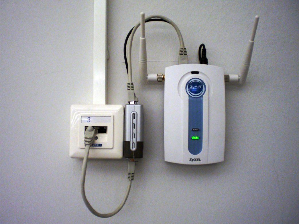 In this configuration, an Ethernet connection includes Power over Ethernet (PoE) (gray cable looping below), and a PoE splitter provides a separate data cable (gray, looping above) and power cable (black, also looping above) for a wireless access point. The splitter is the silver and black box in the middle between the wiring junction box (left) and the access point (right). COURTESY IMAGE